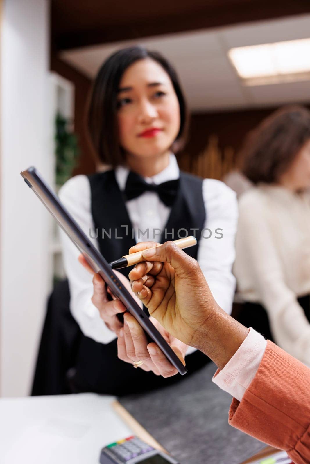 African american woman signing papers to do check in process with receptionist at front desk. Hotel guest filling in registration files at reception, talking to employee about service. Close up.
