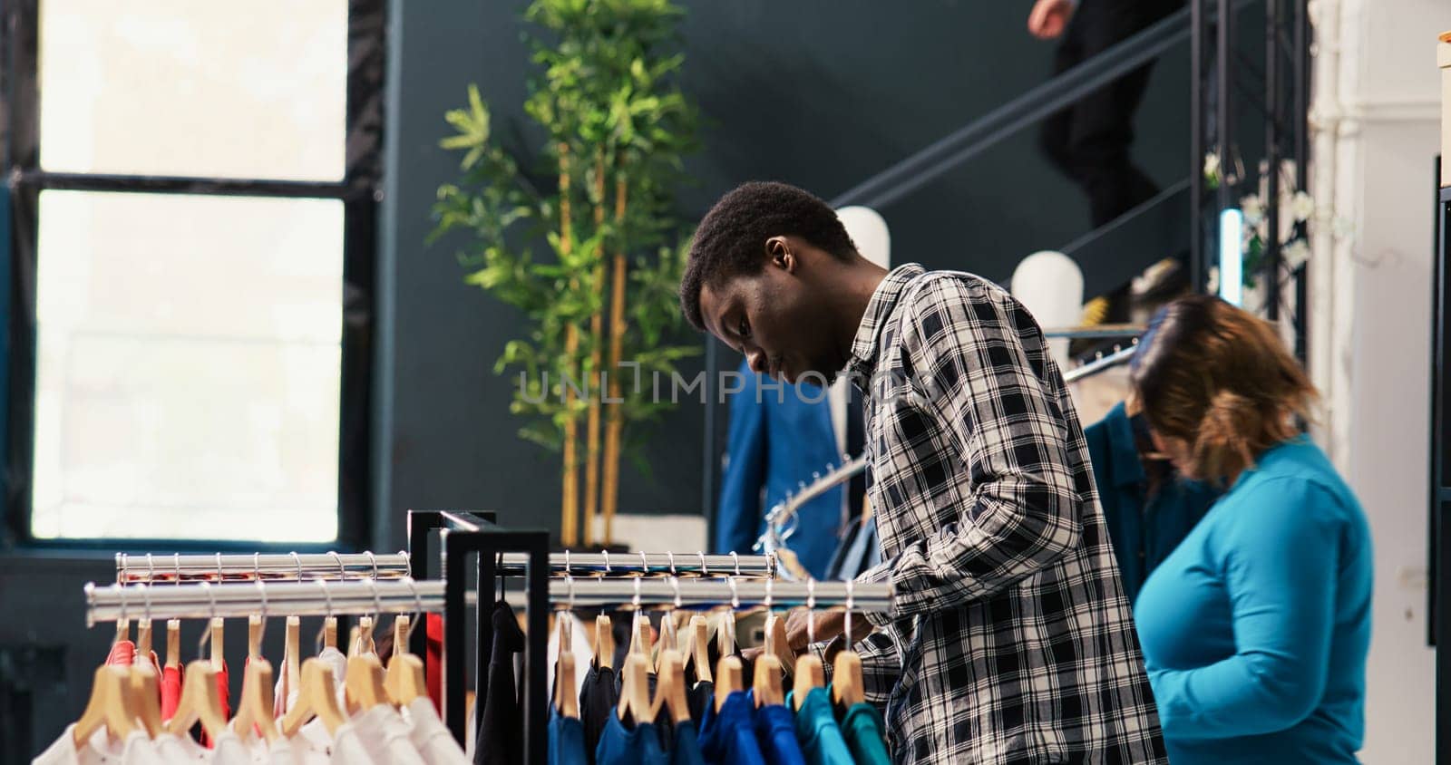 African american shopper analyzing fashionable shirt, checking clothes fabric before buying it. Shopaholic customer shopping for stylish merchandise and accessories in clothing store