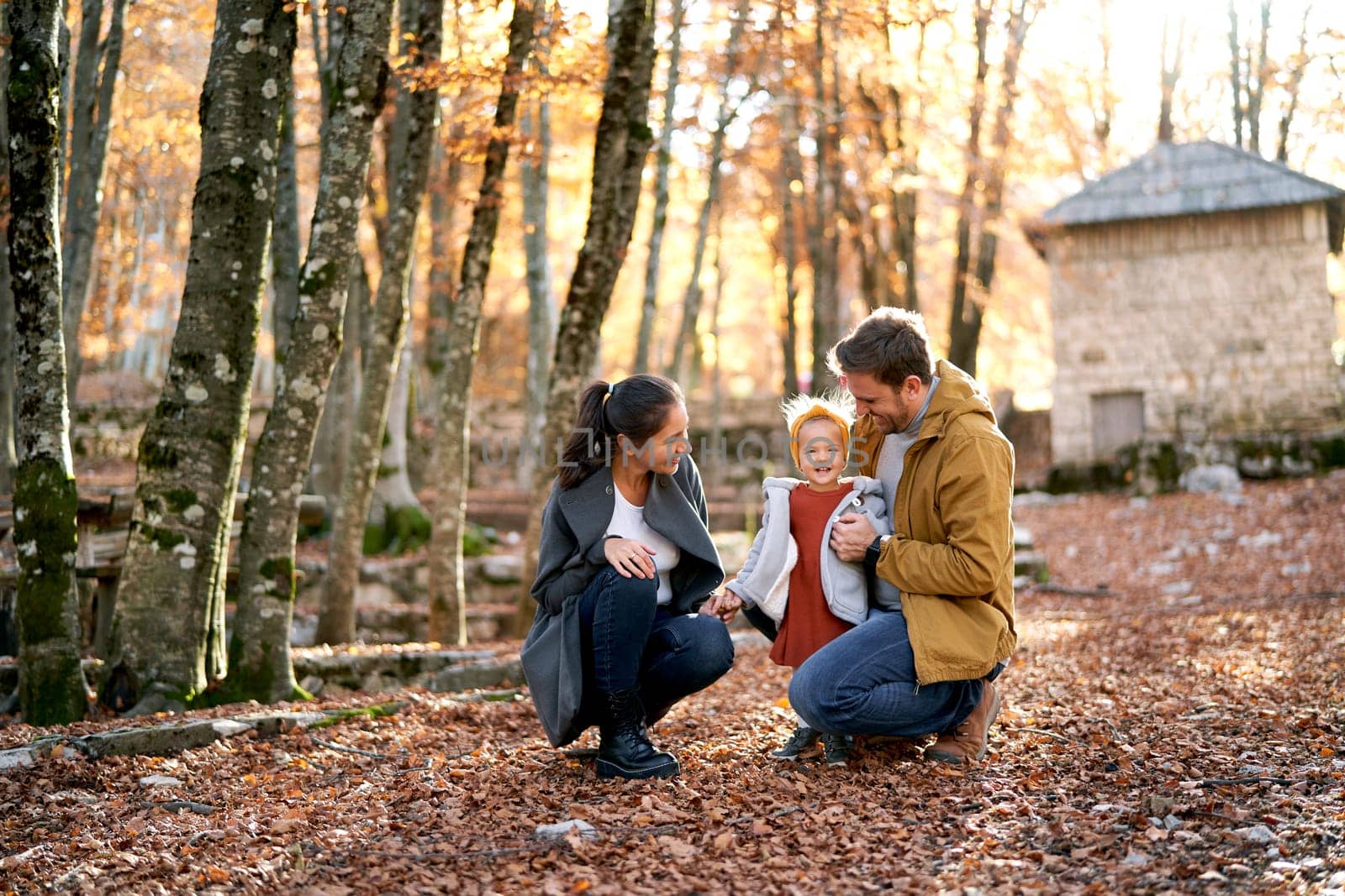 Mom looks at a little girl who is hugged by dad while squatting in the autumn forest. High quality photo