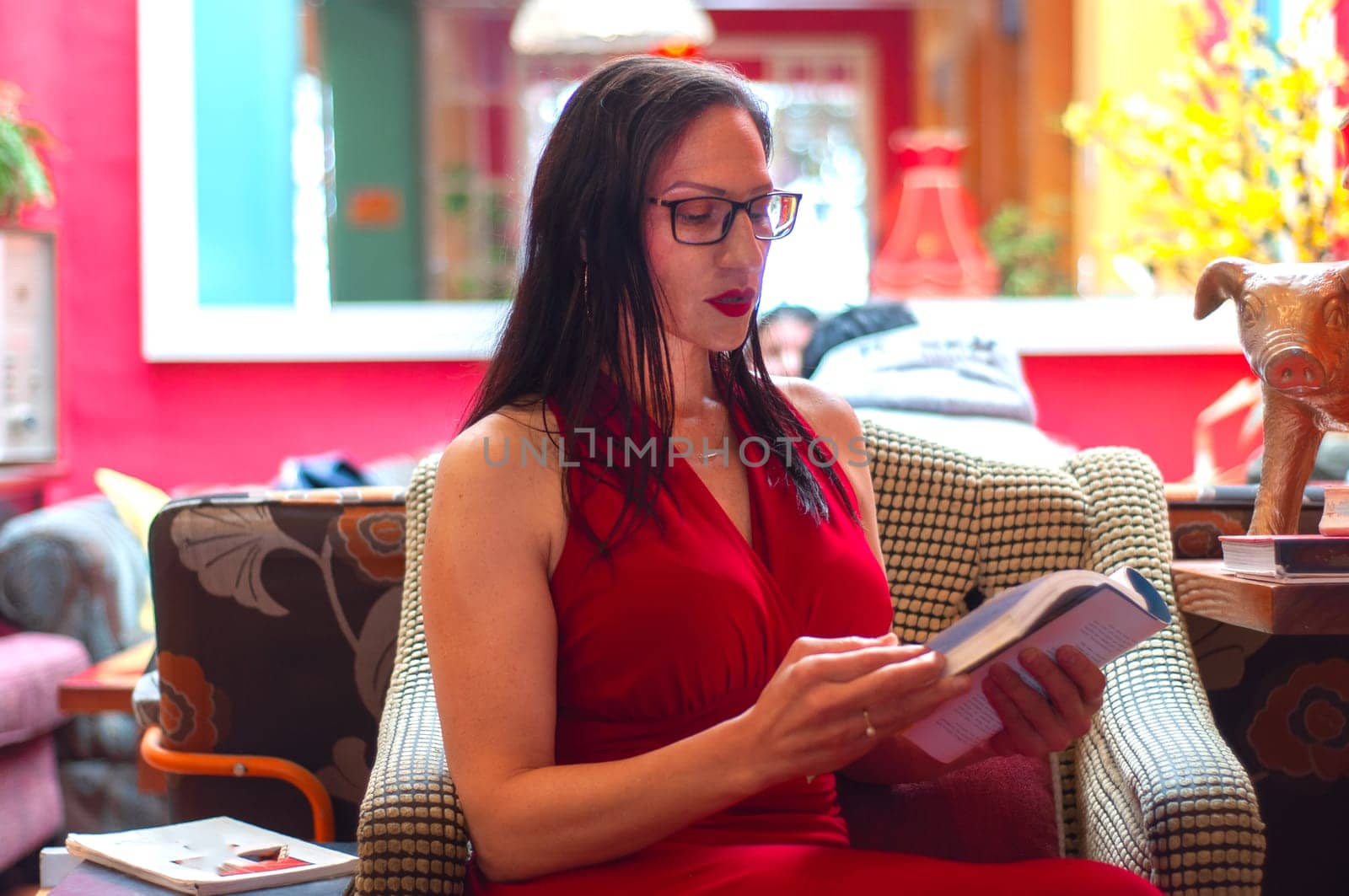 elegant adult woman with glasses and red dress sitting on a sofa reading a book with great attention. book day. High quality photo