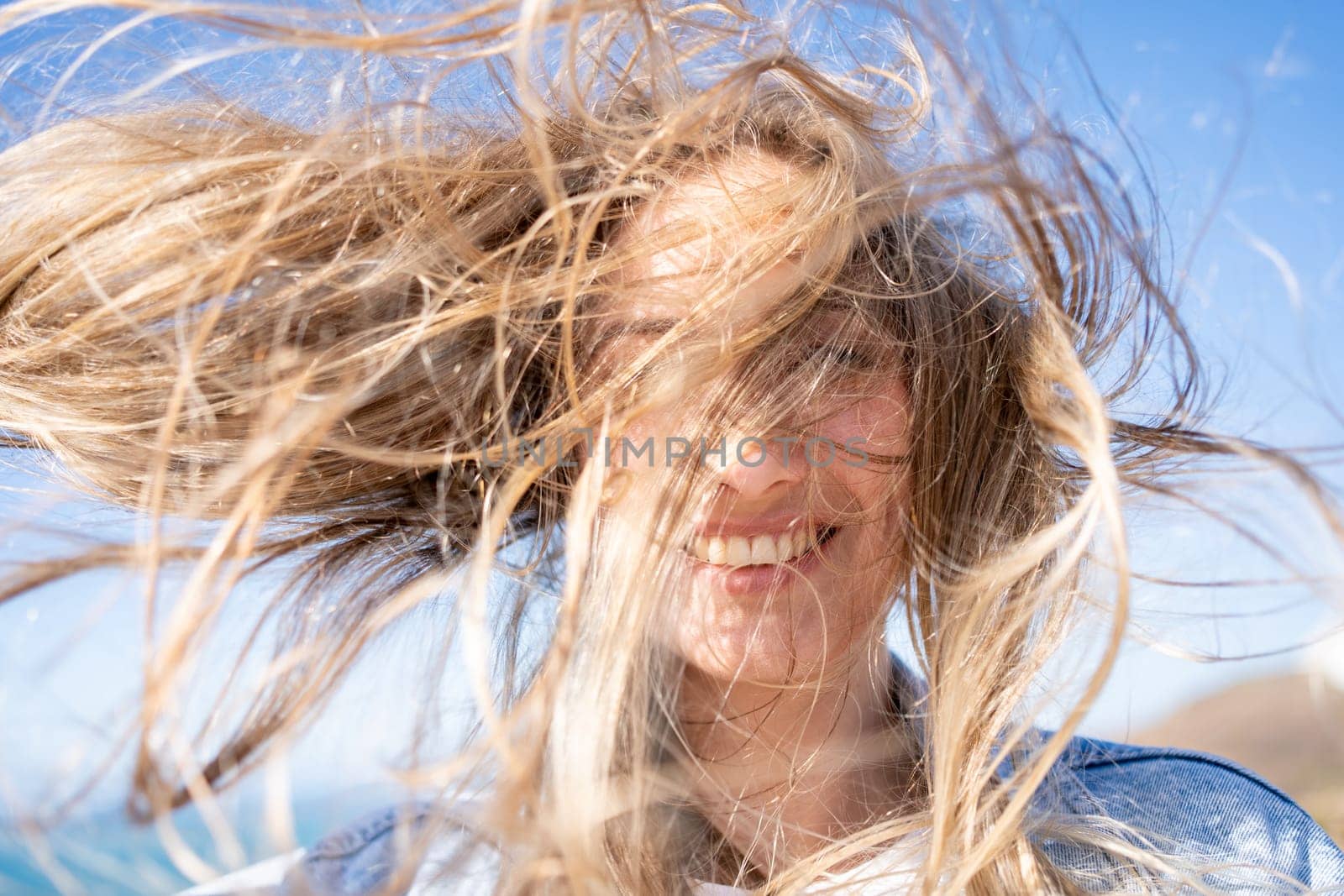 Closeup of young woman face covered with flying hair in windy day. Portrait female with hair blowing in the wind. Wanderlust autumn travel, atmospheric moment