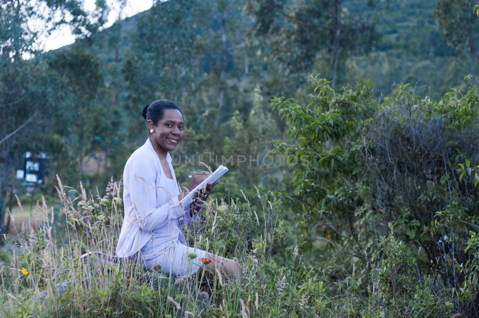 copyspace of an old afro woman sitting on a stone in the middle of the nature with a book in her hand and smiling to the camera, book day by Raulmartin