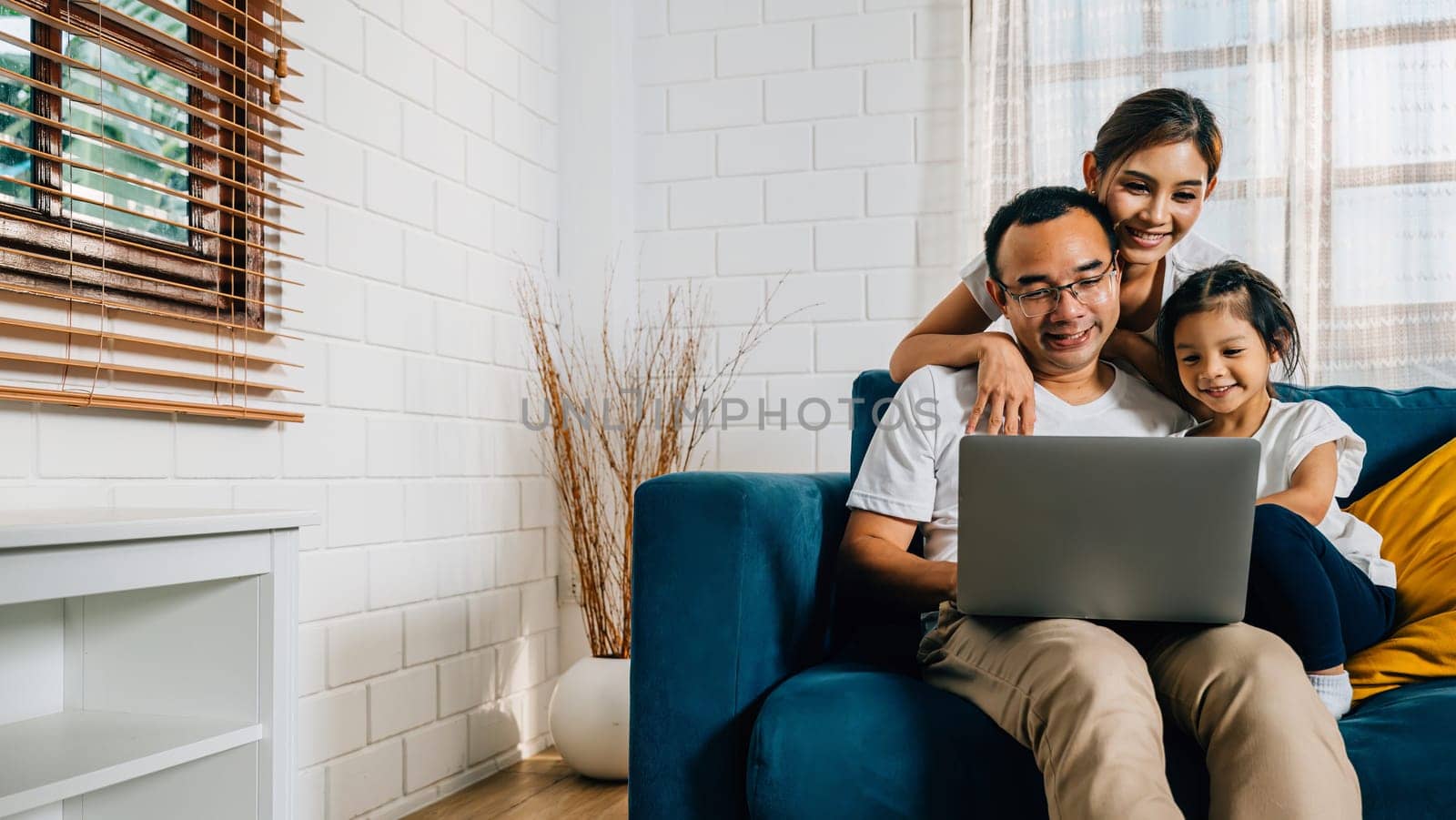 Parents and kids gathered on the couch with a laptop finding happiness in their modern family time by Sorapop