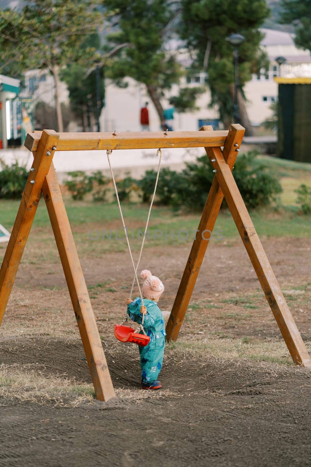 Little girl holds the swing seat behind her to sit on. Back view by Nadtochiy