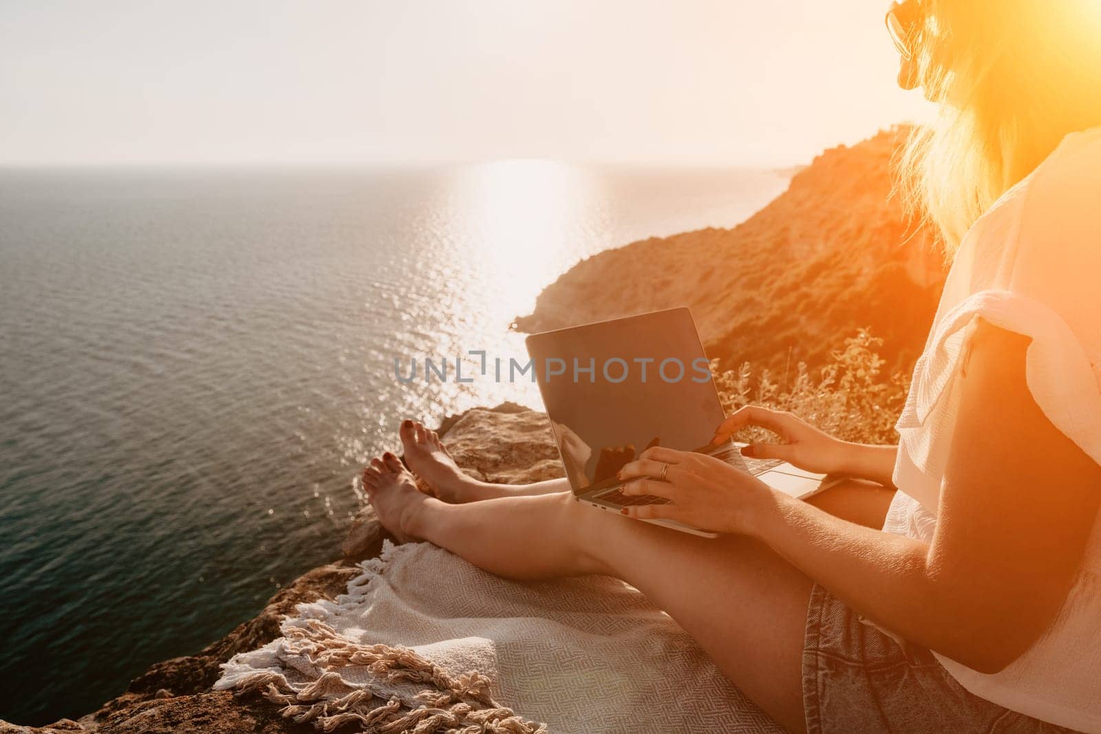 Woman sea laptop. Business woman in yellow hat working on laptop by sea. Close up on hands of pretty lady typing on computer outdoors summer day. Freelance, digital nomad, travel and holidays concept.