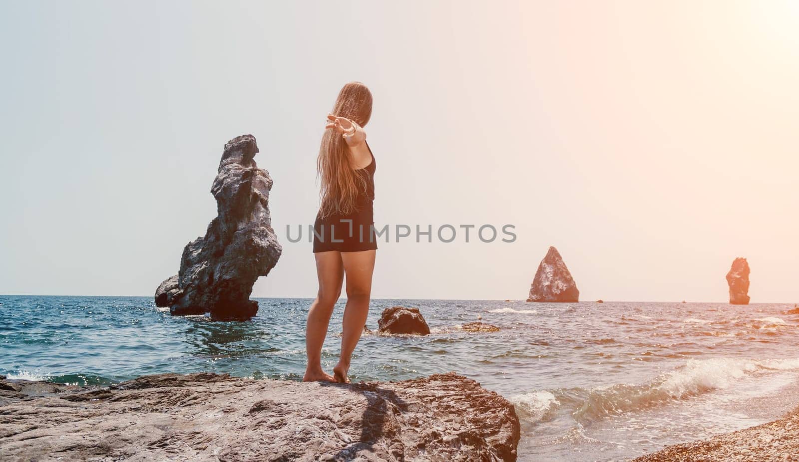 Woman travel sea. Young Happy woman in a long red dress posing on a beach near the sea on background of volcanic rocks, like in Iceland, sharing travel adventure journey