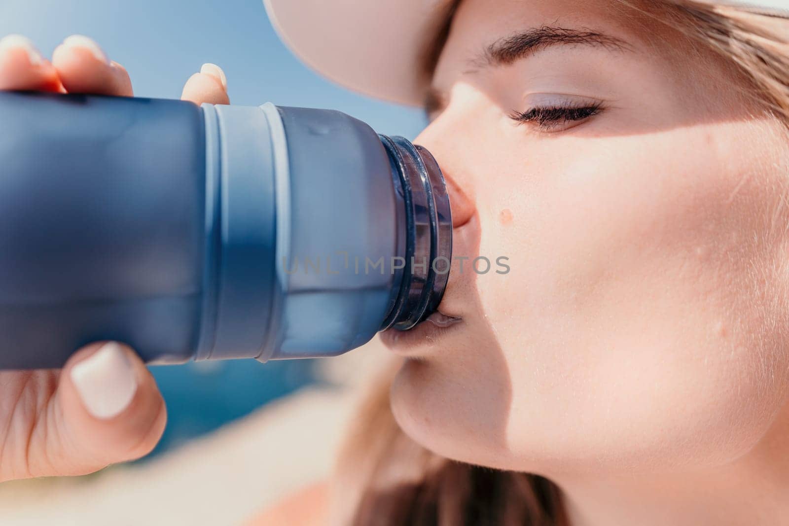 Fintess woman drinking water. Happy, active middle aged woman standing on beach and drinking water after excersise. Concept of lifestyle, sport. Close up.