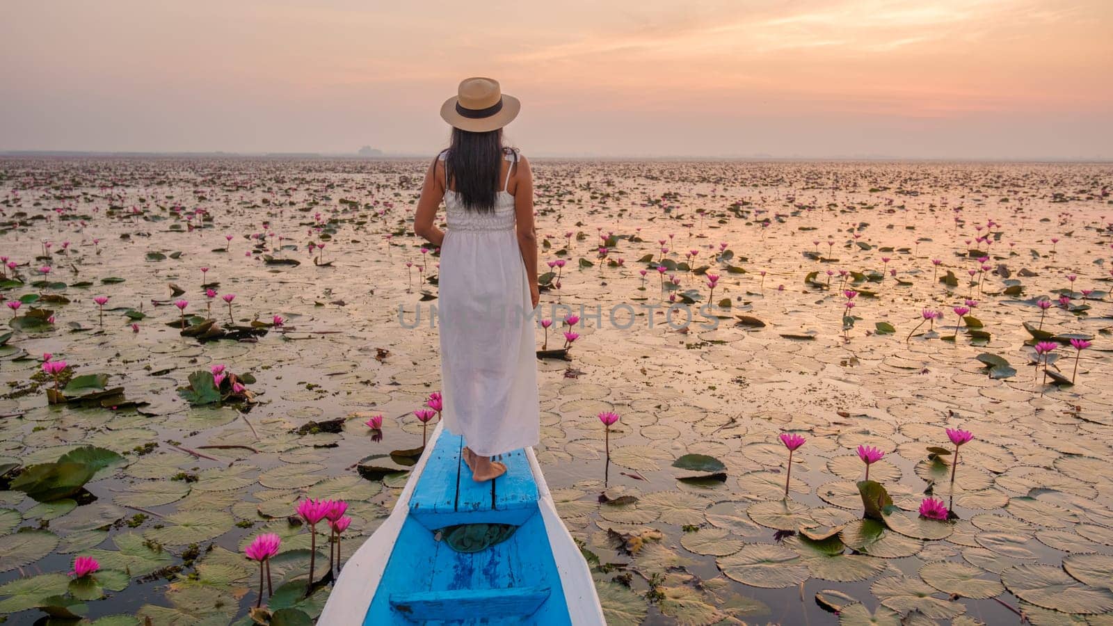The sea of red lotus, Lake Nong Harn, Udon Thani, Thailand. Asian woman with hat and dress on a boat at the red lotus lake in the Isaan