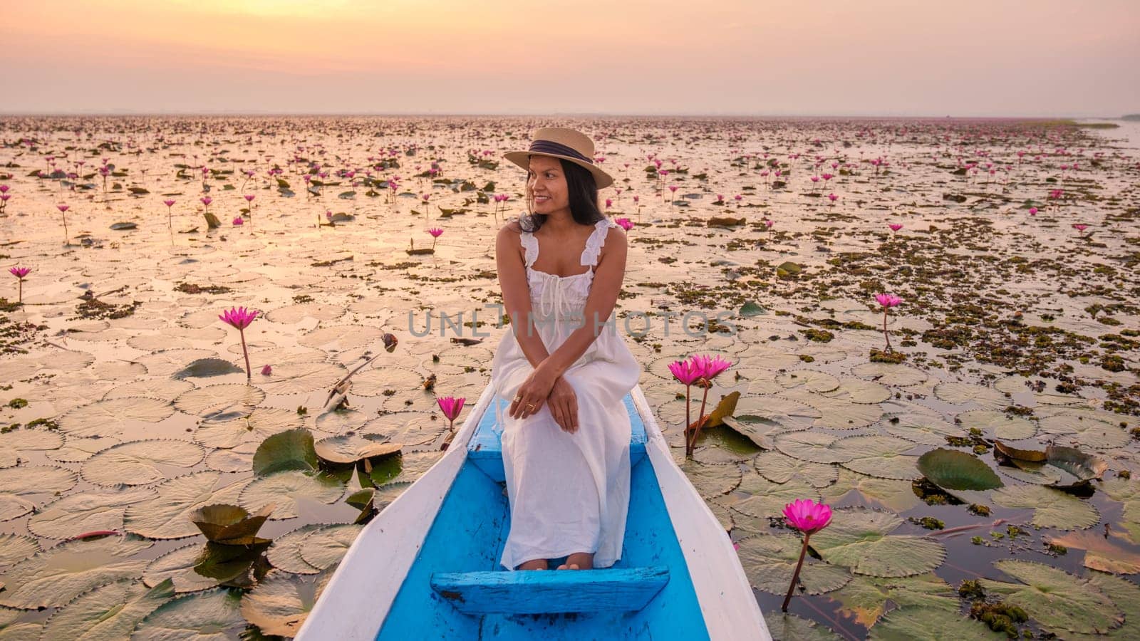 The sea of red lotus, Lake Nong Harn, Udon Thani, Thailand. Asian woman with a hat and dress on a boat at the Red Lotus Lake in the Isaan