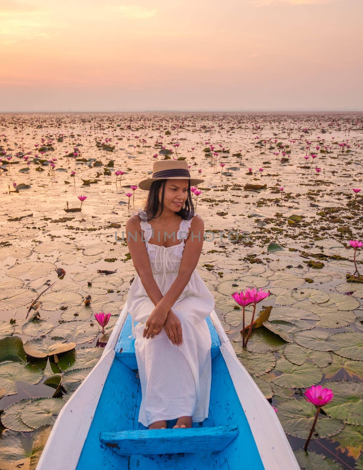 The sea of red lotus, Lake Nong Harn, Udon Thani, Thailand. Asian woman with hat and dress on a boat at the red lotus lake in the Isaan at sunrise