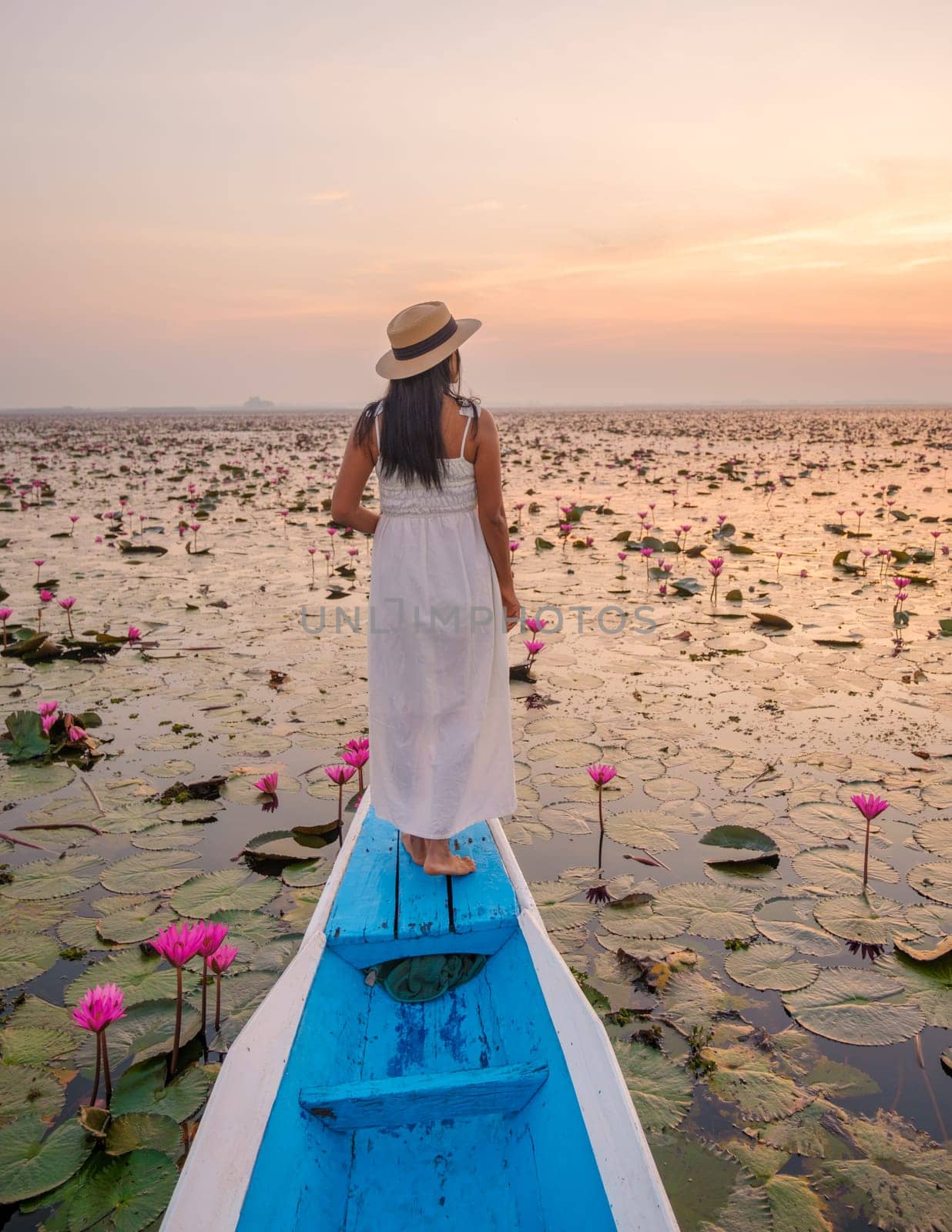 The sea of red lotus, Lake Nong Harn, Udon Thani, Thailand. Asian woman with hat and dress on a boat at the red lotus lake in the Isaan at sunrise