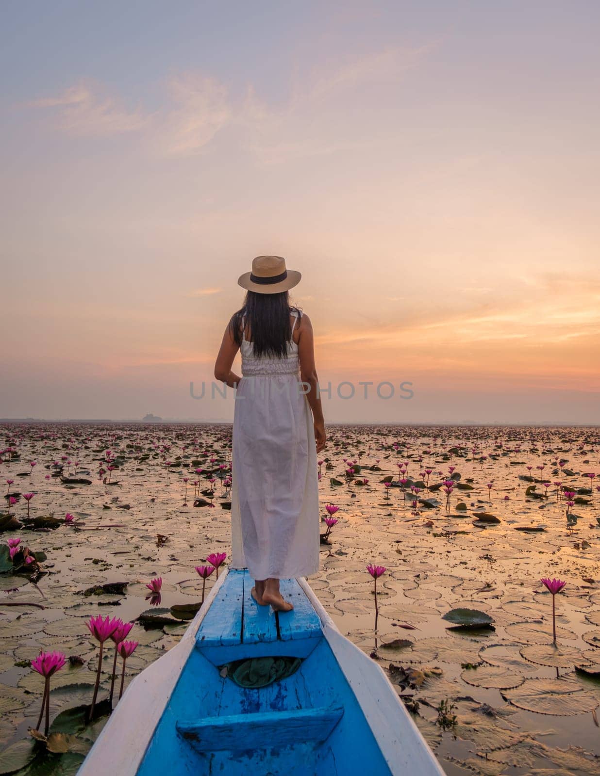 Sunrise at the sea of red lotus, Lake Nong Harn, Udon Thani, Thailand. Asian woman with a hat and dress on a boat at the Red Lotus Lake in the Isaan