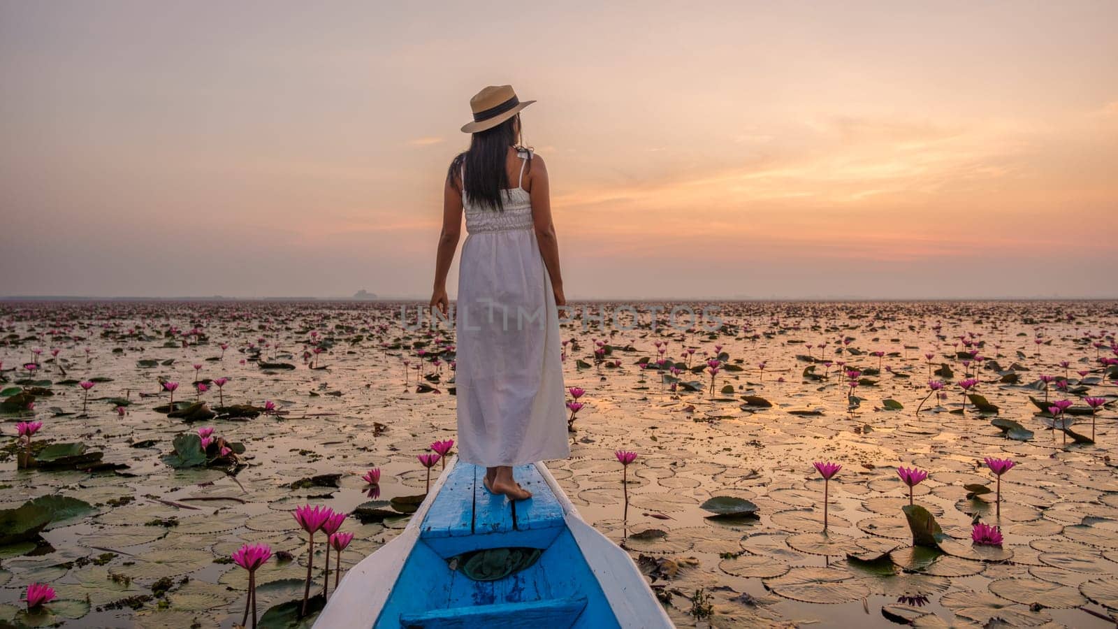 The sea of red lotus, Lake Nong Harn, Udon Thani, Thailand. Asian Thai woman with a hat and dress on a boat at the Red Lotus Lake in the Isaan