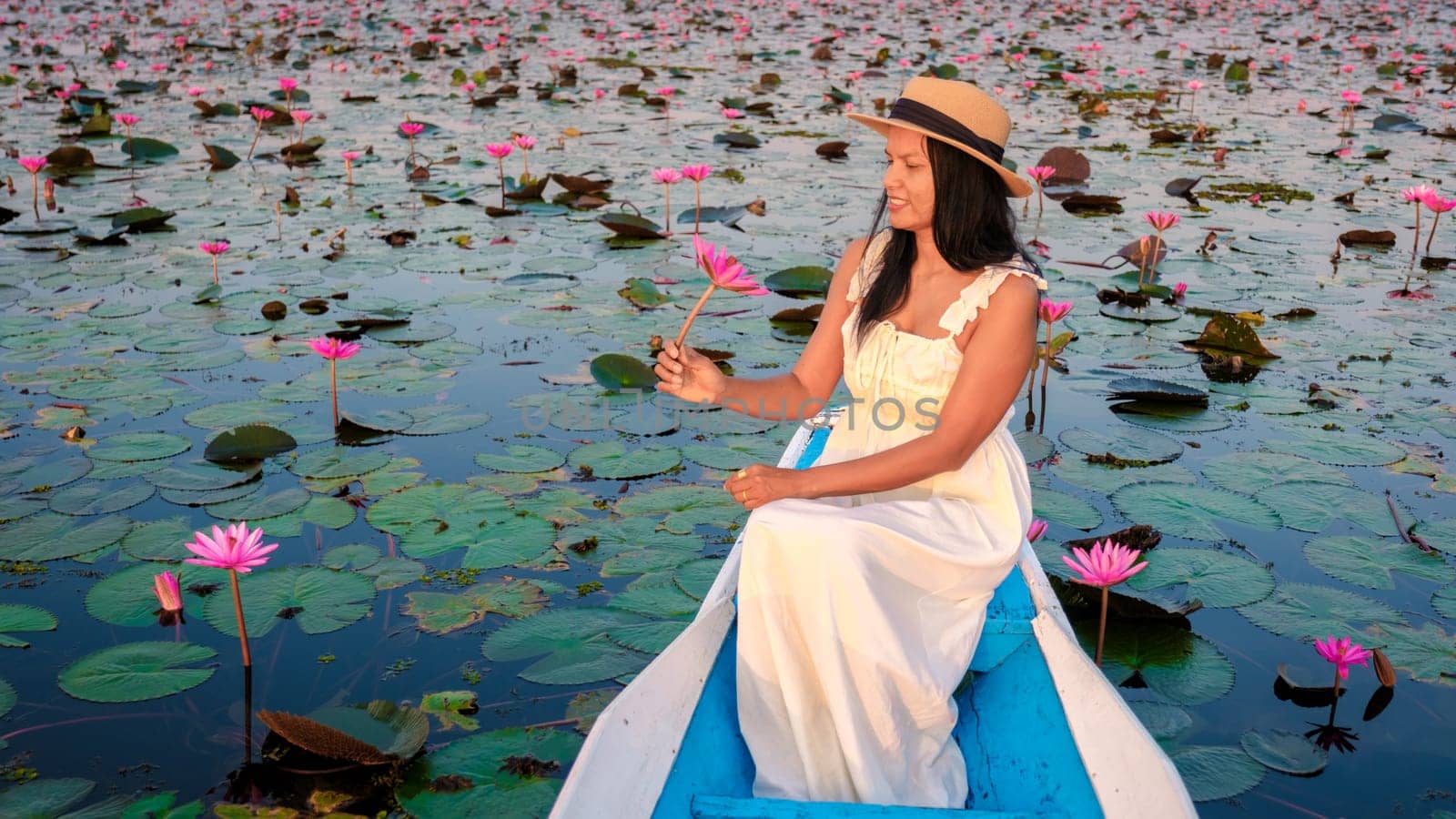 The sea of red lotus, Lake Nong Harn, Udon Thani, Thailand. Asian Thai woman with a hat and dress on a boat at the Red Lotus Lake in the Isaan