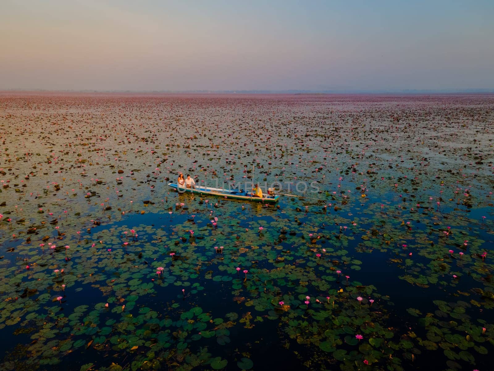 Sunrise at the sea of red lotus, Lake Nong Harn, Udon Thani, Thailand, a couple of men and woman in a boat at sunrise at the Red Lotus Lake in the Isaan