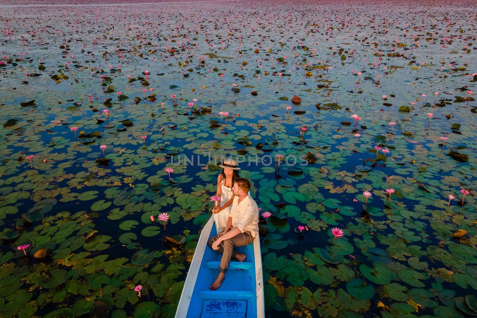 Drone aerial view at the sea of red lotus, Lake Nong Harn, Udon Thani, Thailand, a couple of men and woman in a boat at sunrise at the Red Lotus Lake in the Isaan