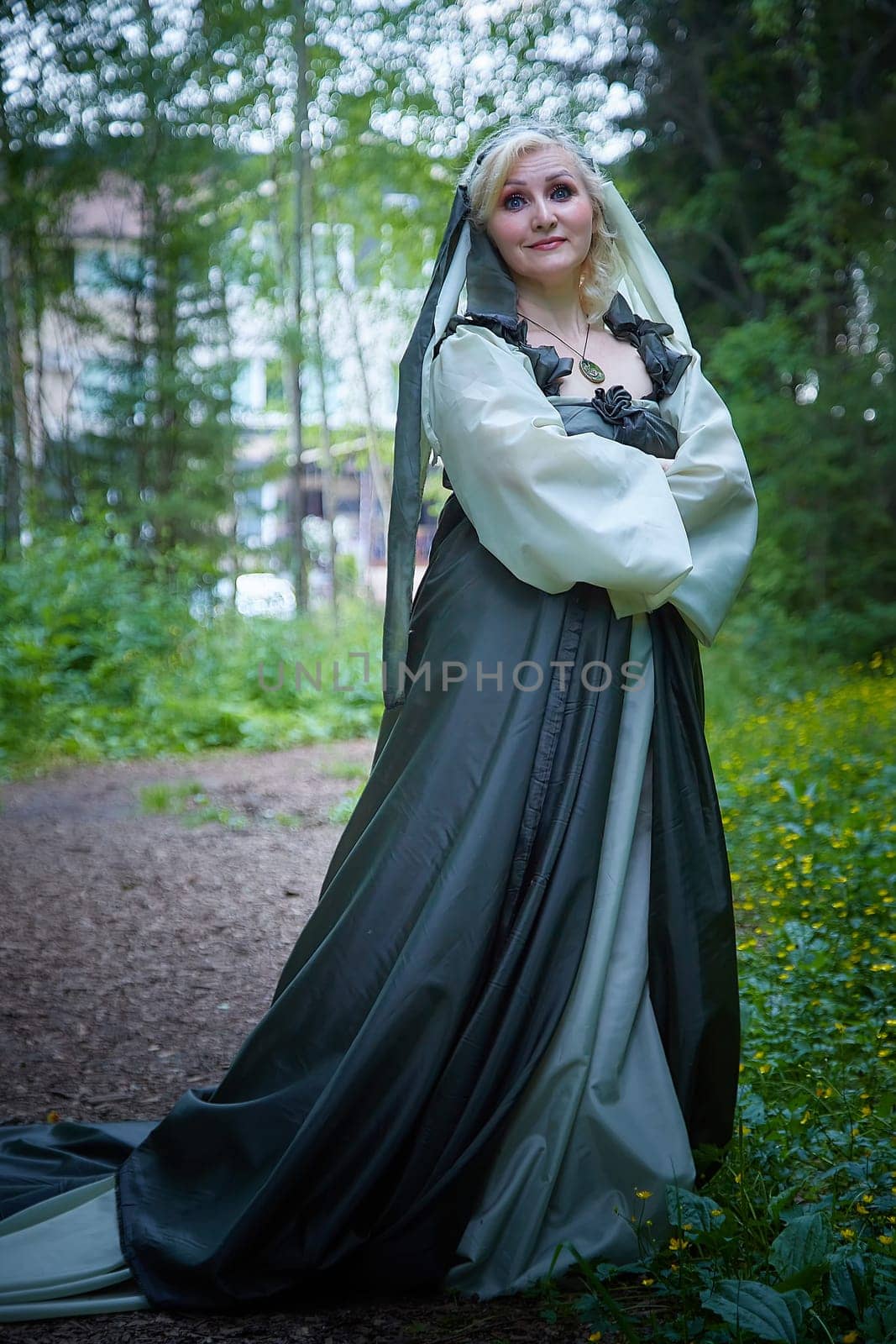 Adult mature woman 40-60 in a green long fairy dress in forest. Photo shoot in style of dryad and queen of nature. Fairy in beautiful green summer forest. Concept of caring for nature