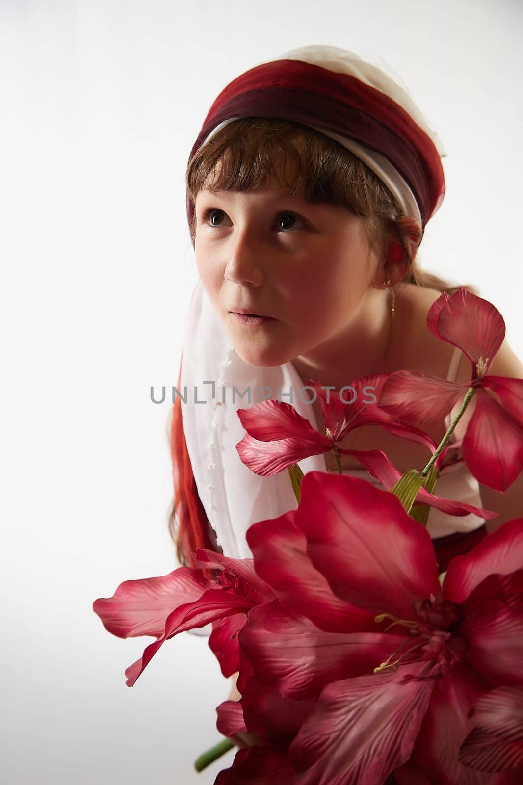 Portrait of Little girl in a stylized Tatar national costume with flowers on a white background in the studio. Photo shoot of funny young teenager who is not professional model by keleny