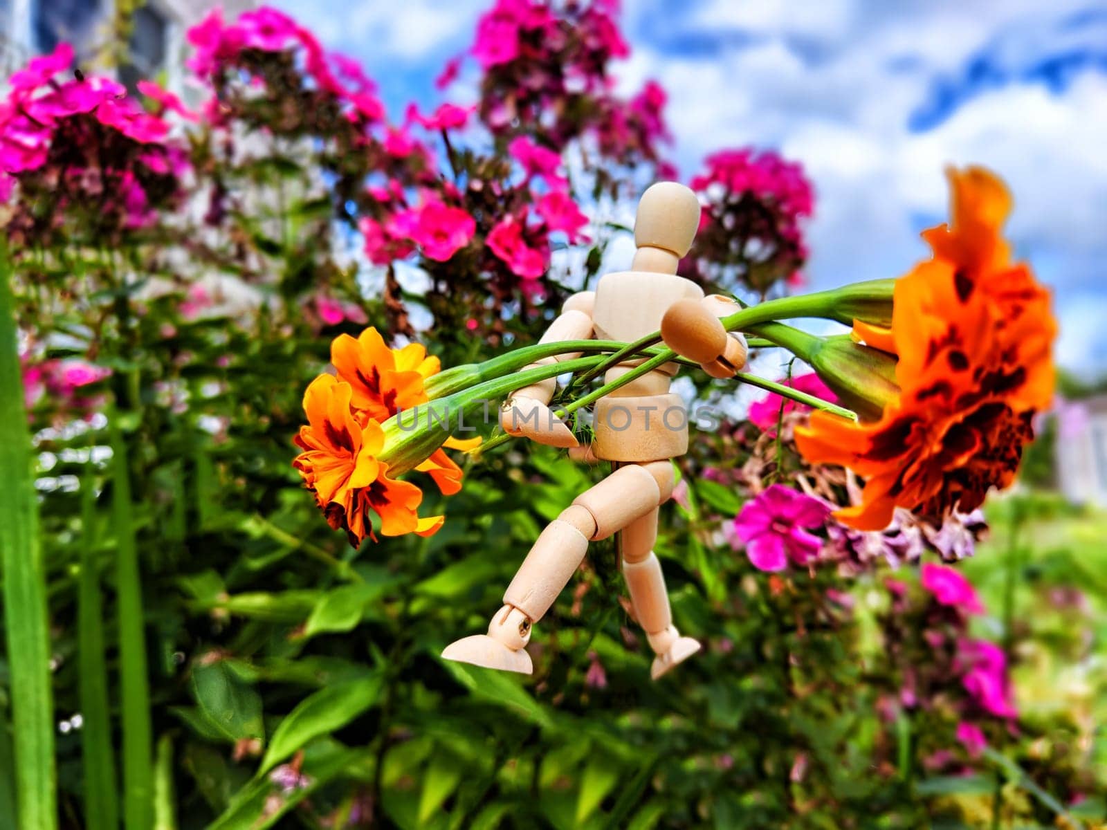 Wooden toy man with flowers against background grass in nature. Concept of holiday, gift bouquet, Valentine's Day, proposal, engagement, declaration of love, Mother's Day. Caring, loving, romantic by keleny