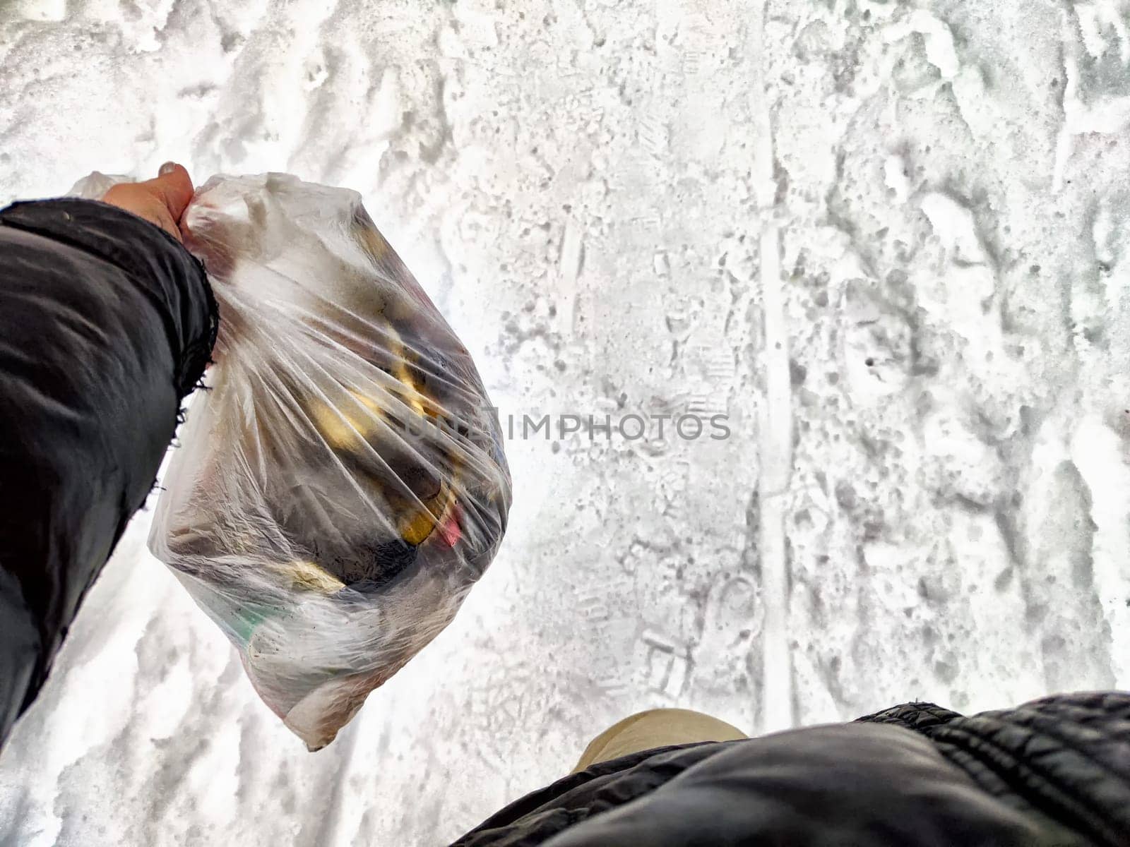 Bag of garbage in hand of woman and snow in forest on the background. A girl cleans up the trash after picnic. A tourist is going to throw garbage in nature. The concept of environmental pollution