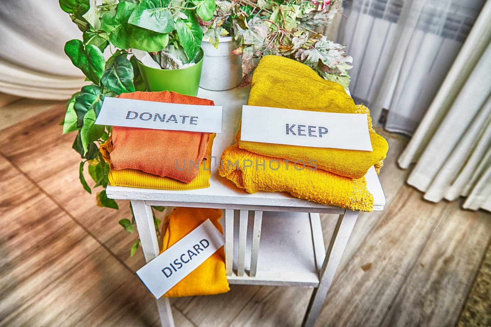 Signs with the words keep, donate, discard and fashion clothes folded in stacks in cozy room. The concept of cluttering and decluttering. Background