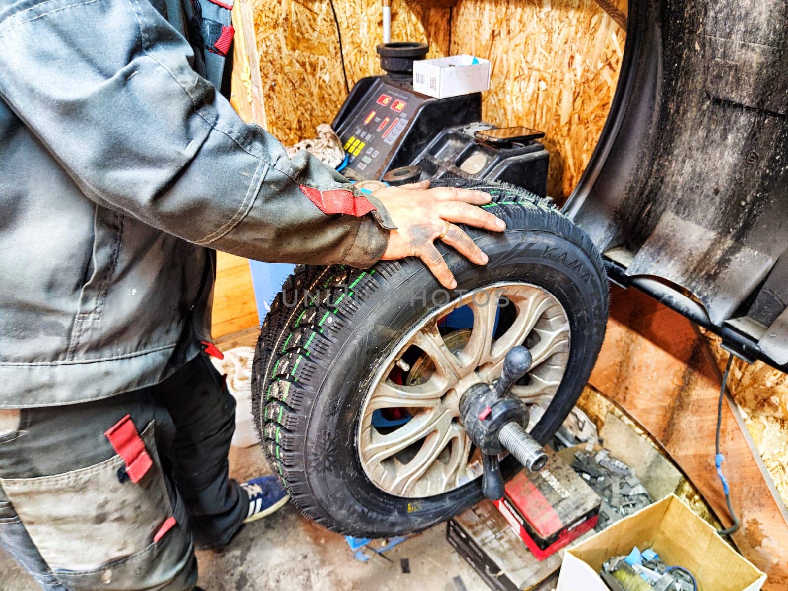 Ishim, Russia - November 27, 2023: A mechanic repairs a car wheel and makes a tire in a dirty garage. Replacement of summer wheels, tires for winter indoors by keleny