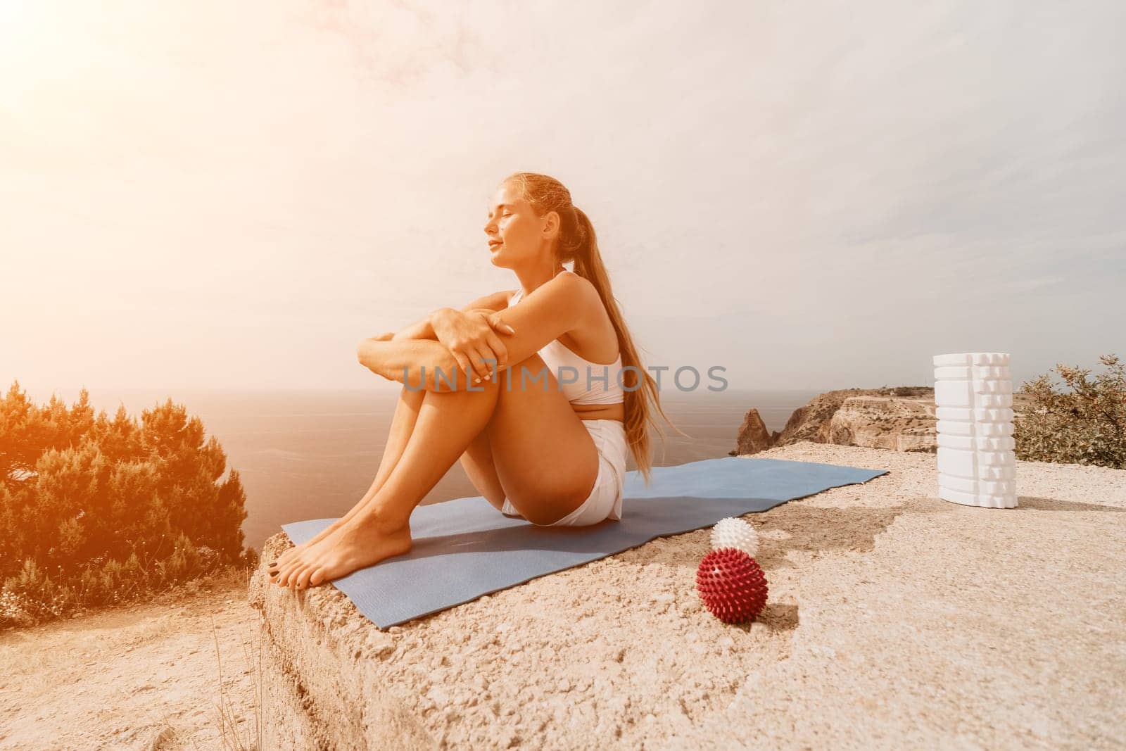 Middle aged well looking woman with black hair doing Pilates with the ring on the yoga mat near the sea on the pebble beach. Female fitness yoga concept. Healthy lifestyle, harmony and meditation.