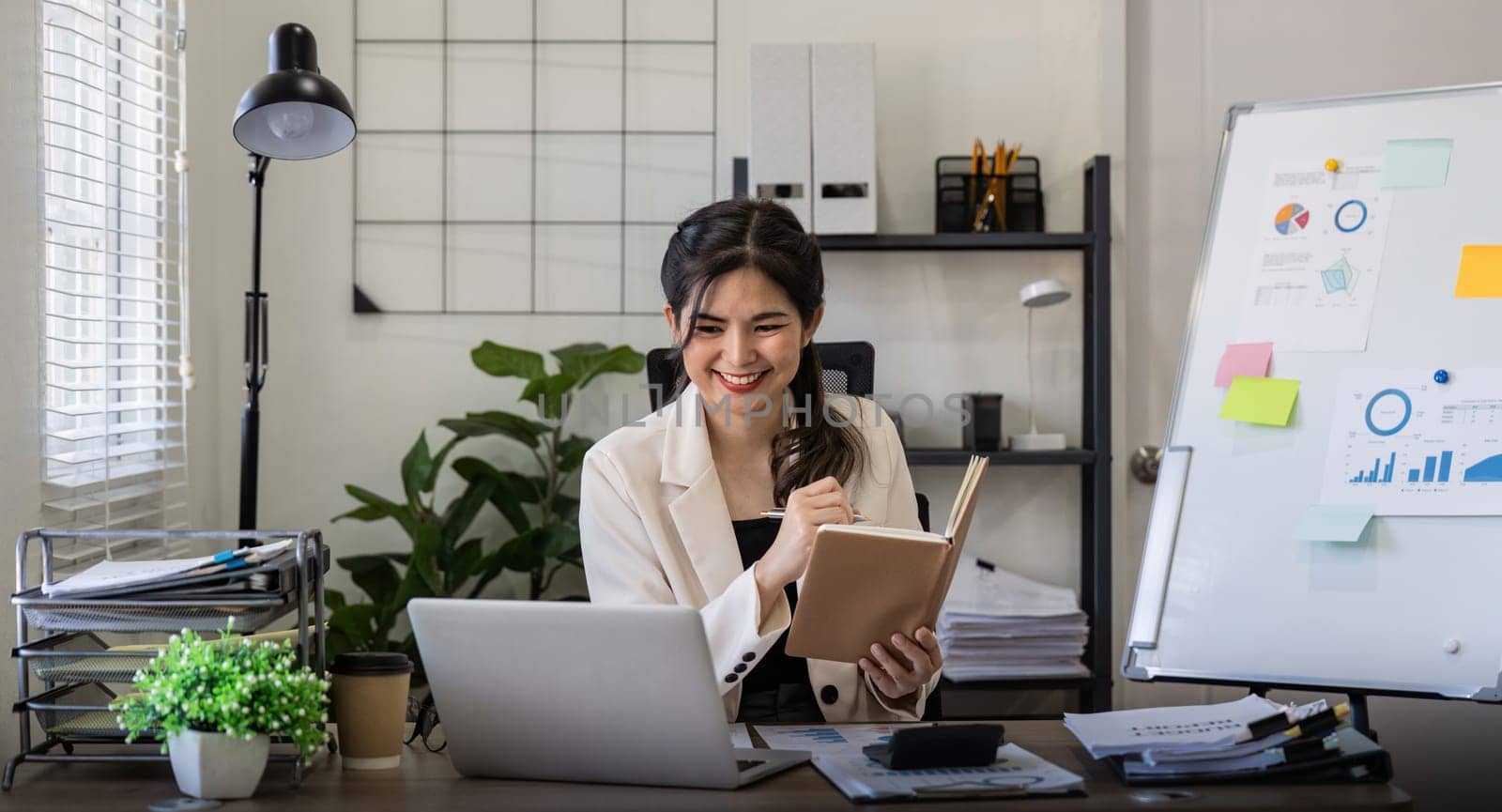 Business woman writing in a office with planning note and corporate laptop. Employee and work planner book with company paperwork.