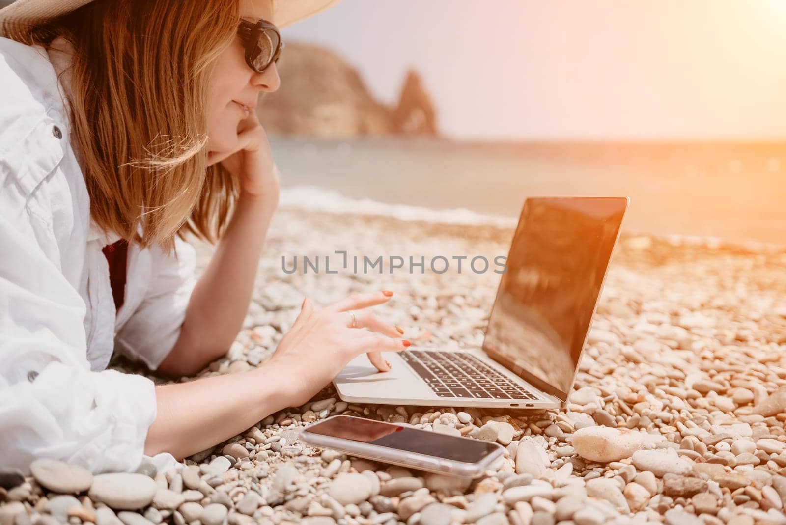 Woman sea laptop. Business woman in yellow hat working on laptop by sea. Close up on hands of pretty lady typing on computer outdoors summer day. Freelance, digital nomad, travel and holidays concept. by panophotograph