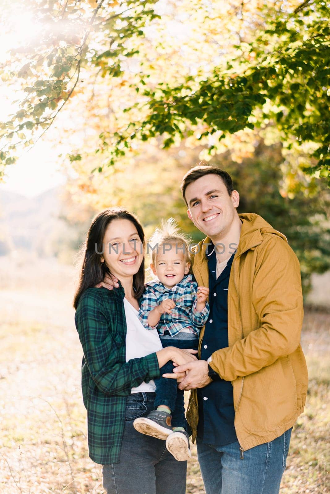 Smiling dad hugging mom with a little girl in her arms while standing in the forest. High quality photo