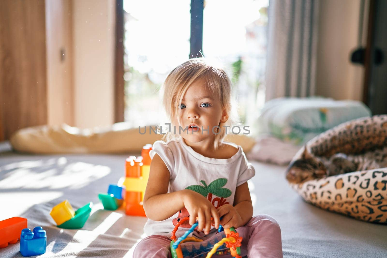 Little girl collects puzzle rattle sitting on the bed by Nadtochiy