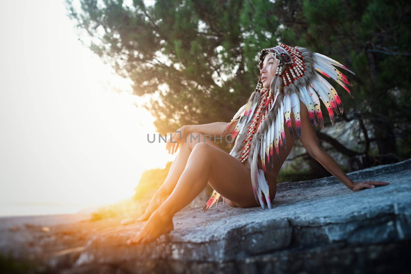 Naked sexy girl in Native American headdresses on the background of nature in beautiful sunset light