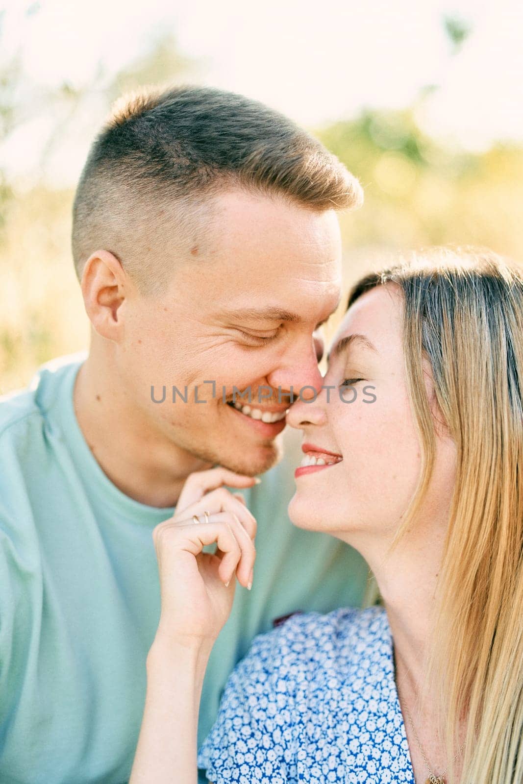 Smiling husband touches wife nose with his nose while sitting hugging in field. High quality photo