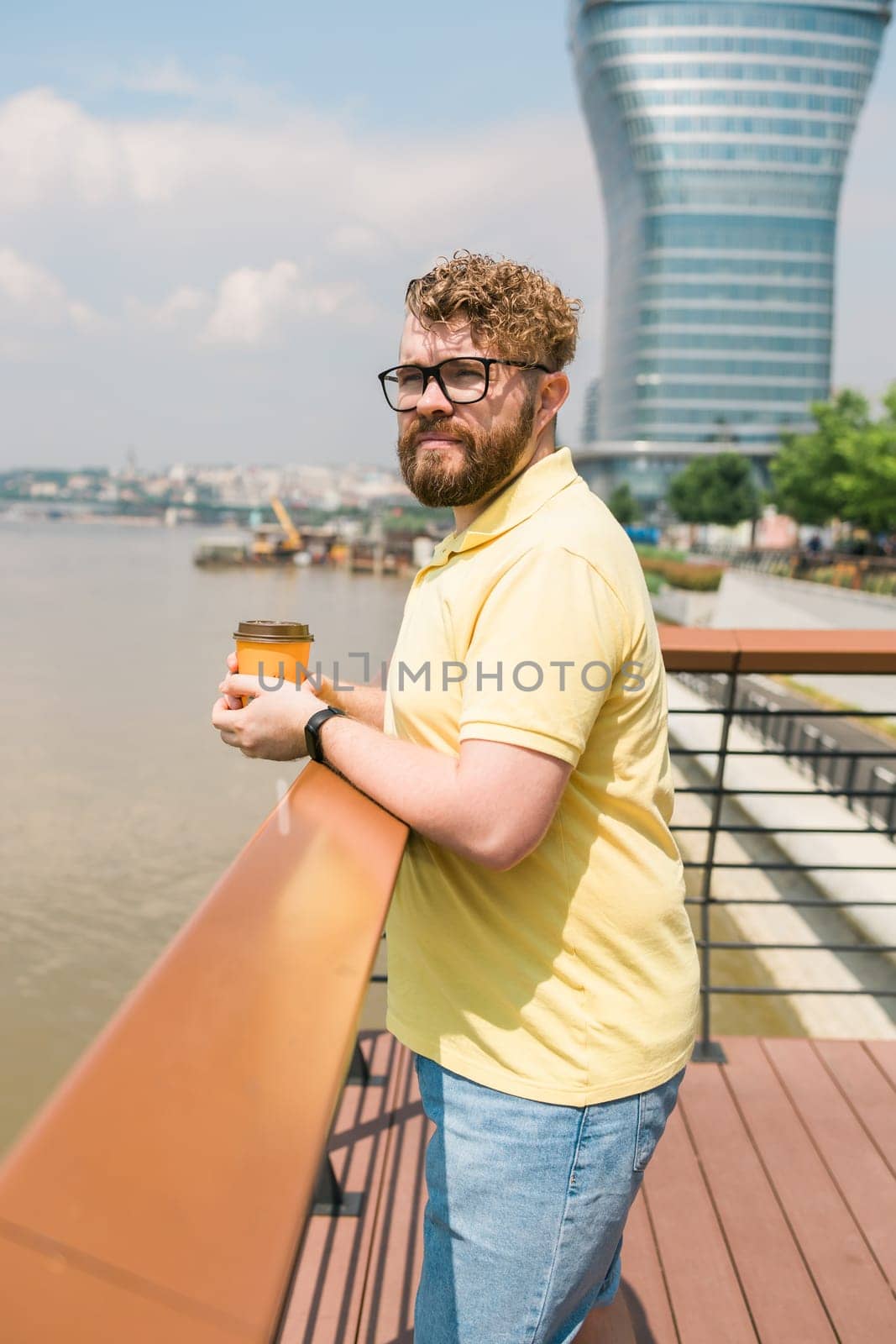 Bearded man holding coffee to take away at early morning in sunny park near river in Belgrade city by Satura86