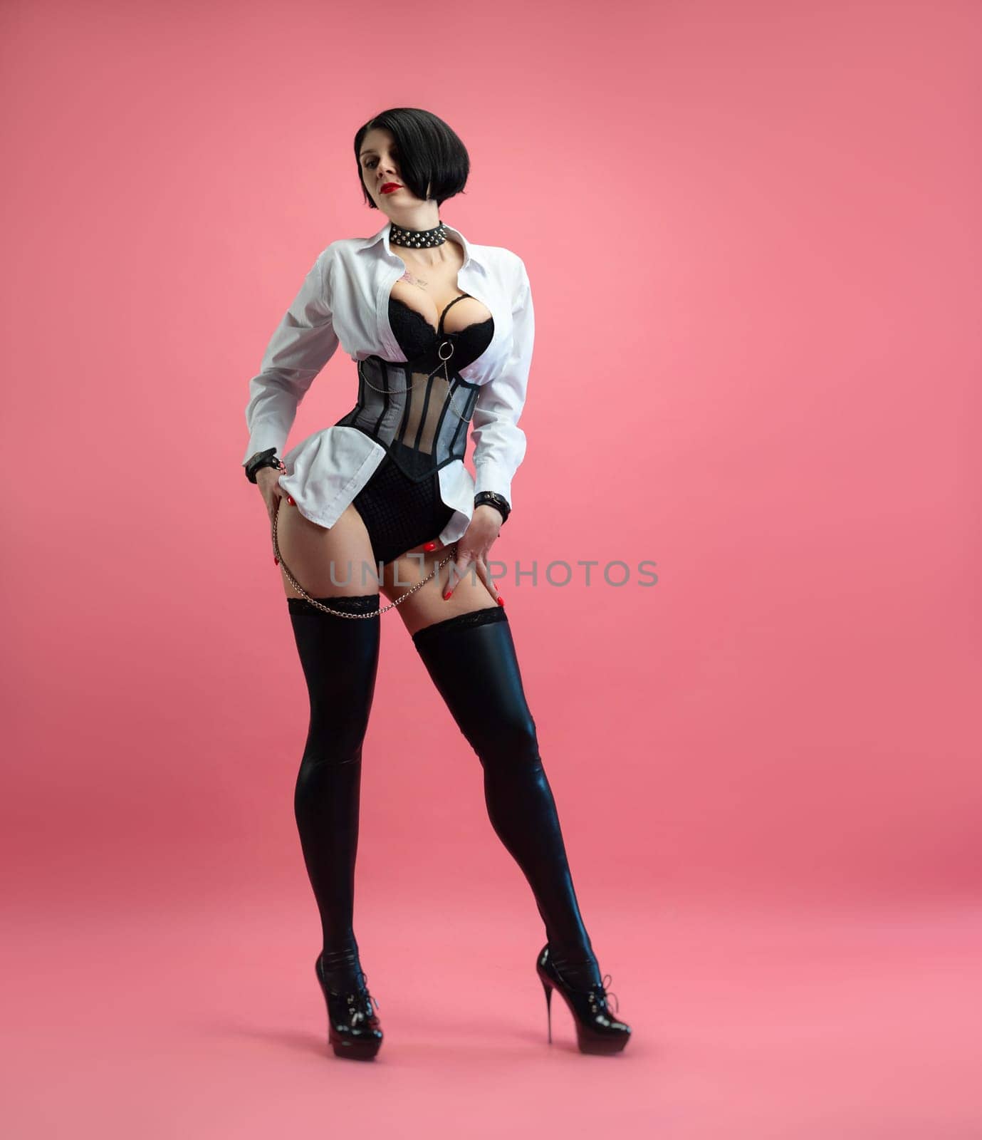 sexy woman with glasses, in a BDSM mistress costume in stockings, posing sexually on pink copy paste background