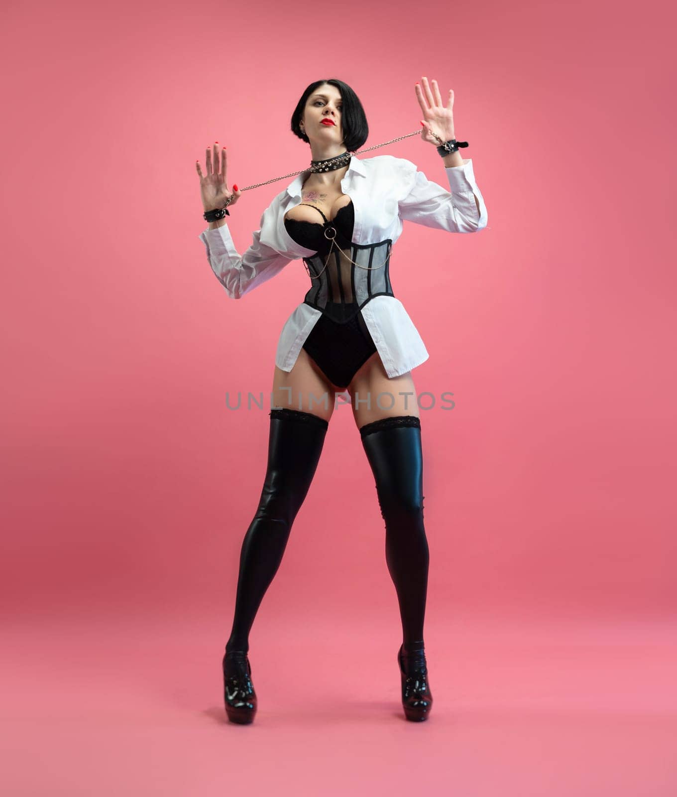 sexy woman with glasses, in a BDSM mistress costume in stockings, posing sexually on pink copy paste background
