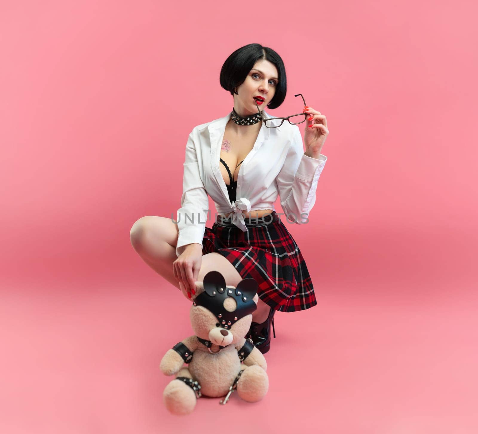 BDSM teddy bear in the hands of a sexy woman in a schoolgirl costume for sexual role-playing games on a pink background, copy paste, a banner for a sex shop