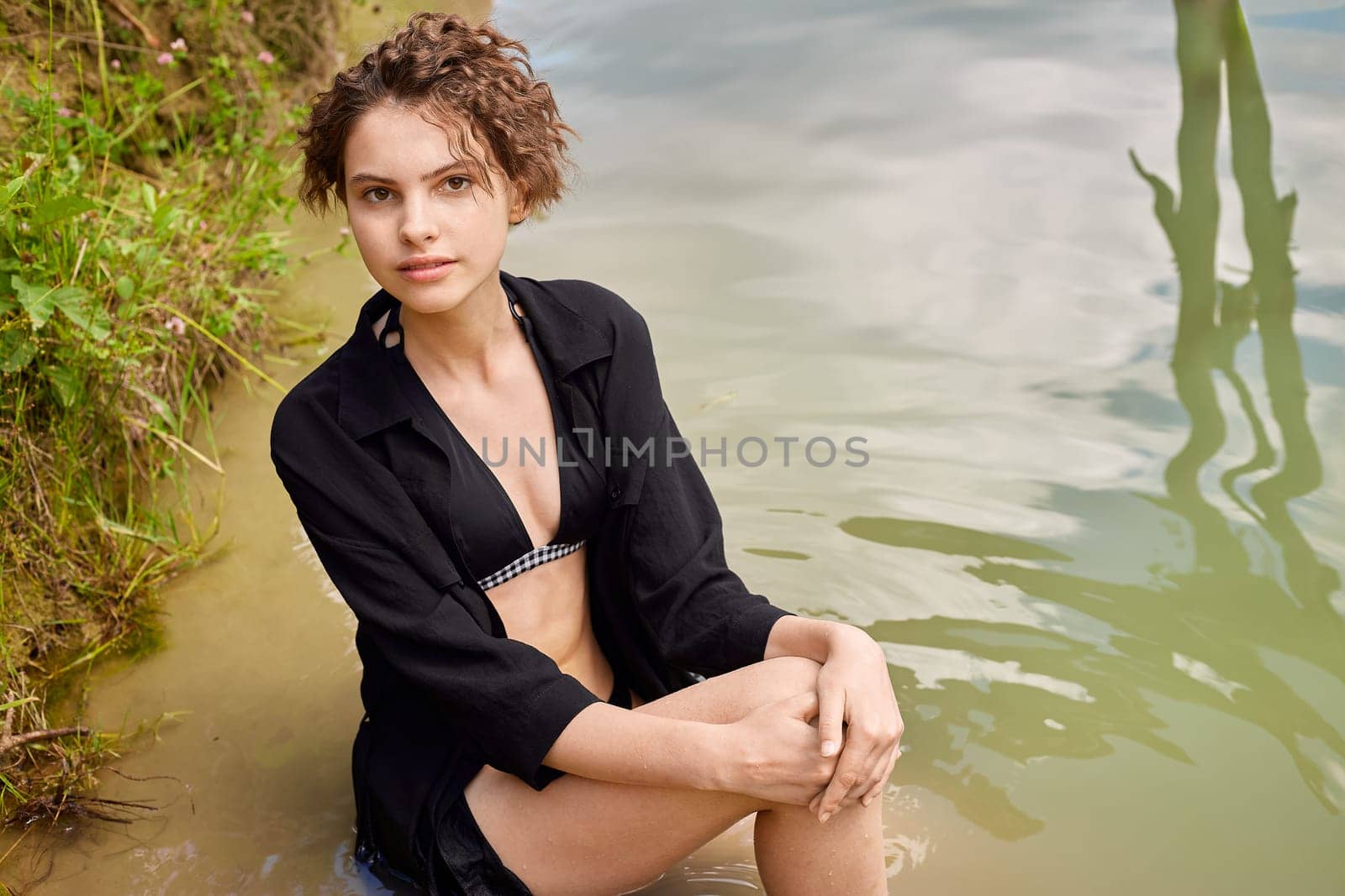 Young woman in a dark dress sits in the water.