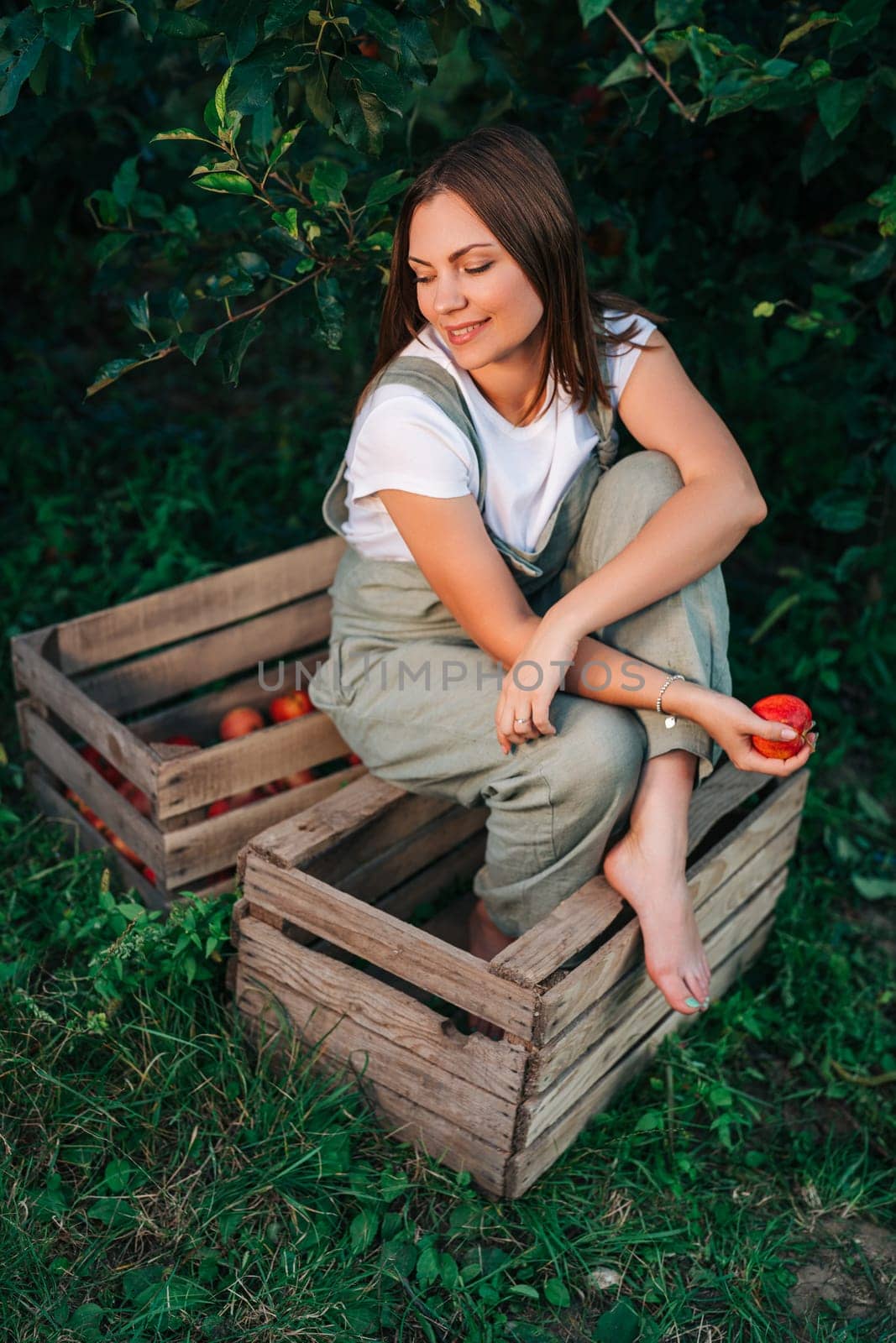 Woman with red juicy apple from tree in own home countryside orchard. Happy gardener, young farmer style. Healthy lifestyle. High quality