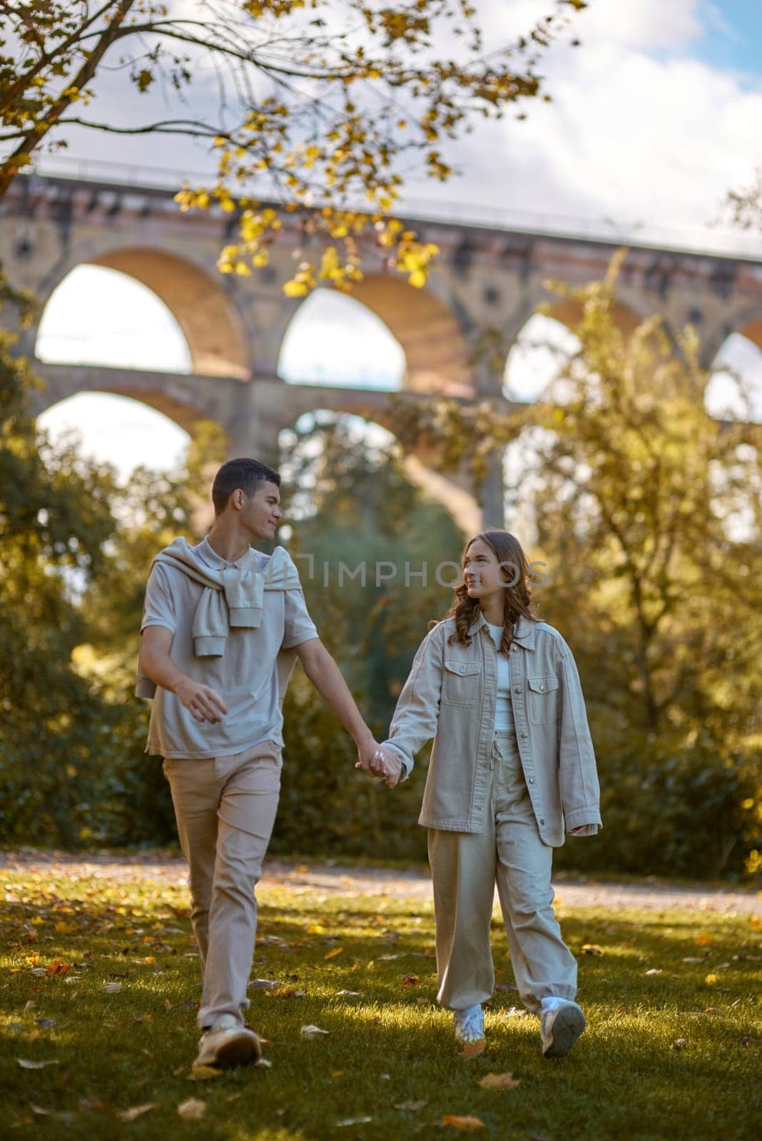 Young couple in love walking in the autumn park holding hands looking in the sunset. Closeup of loving couple holding hands while walking at sunset. The hands of the male and female lovers who hold hands walk forward high with blurred background by Andrii_Ko