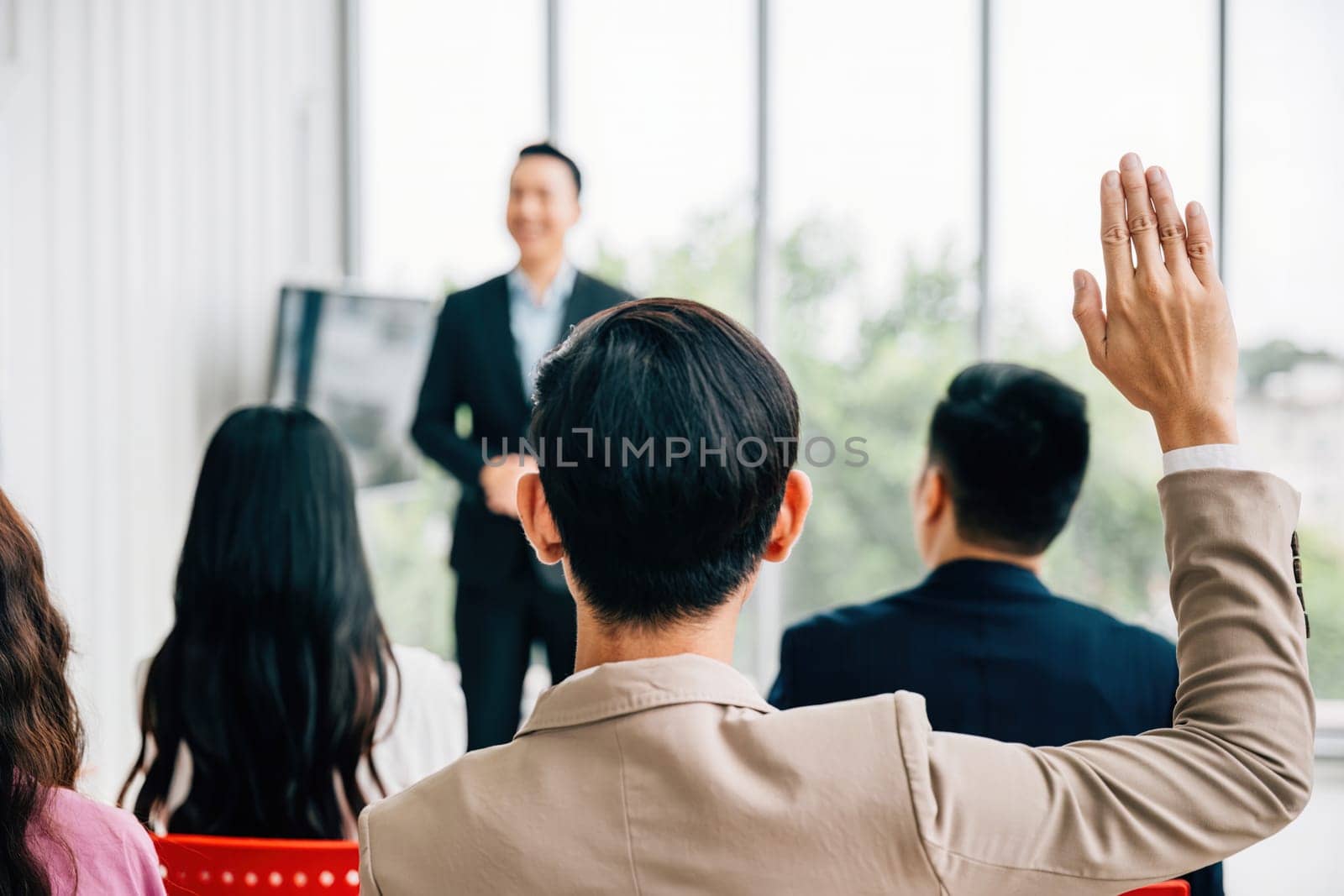 In a conference, hands are raised for questions, reflecting audience engagement and interactive learning. A diverse group participates in a workshop or seminar, fostering teamwork and discussion by Sorapop