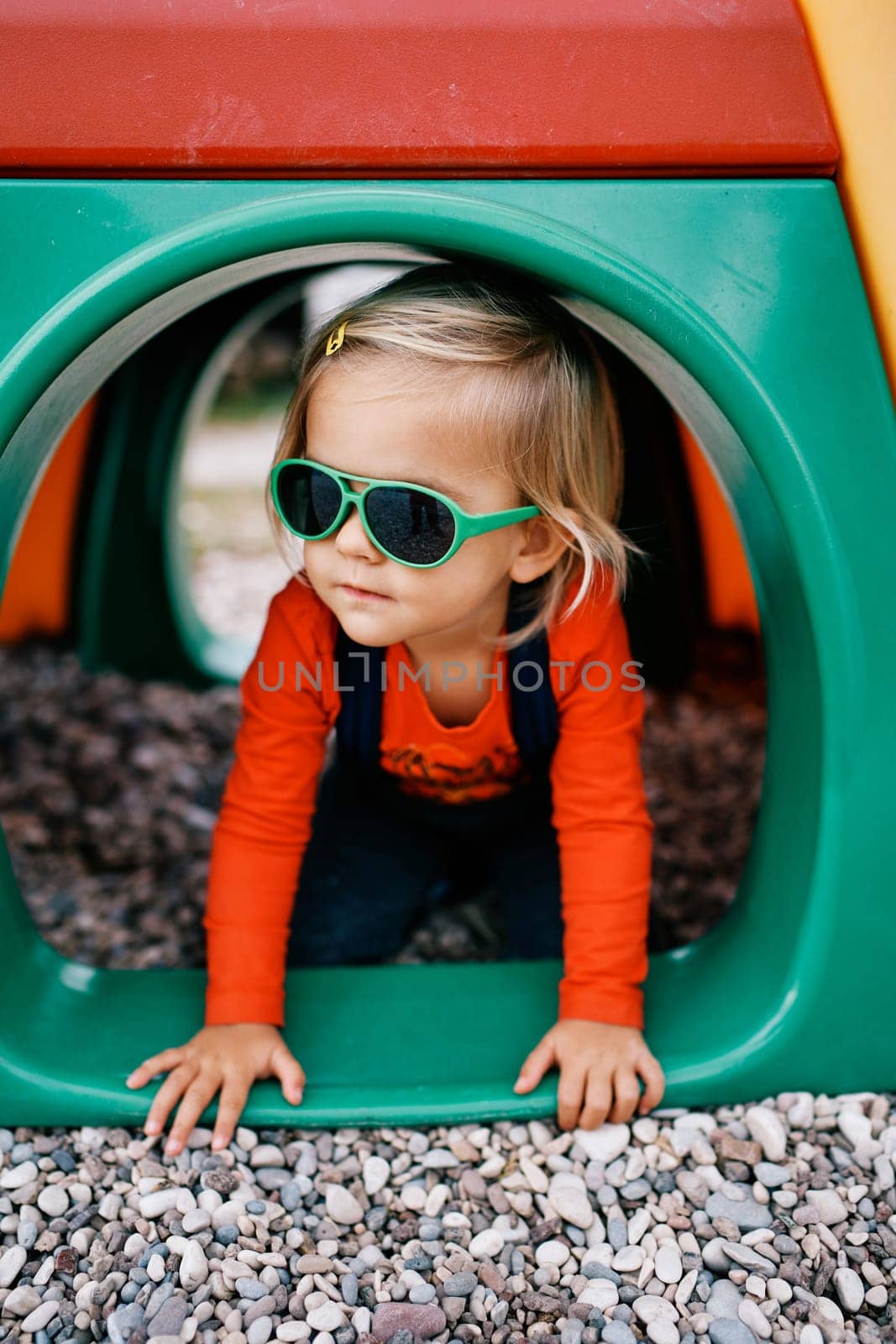 Little girl sitting on her knees in a pipe at the playground. High quality photo