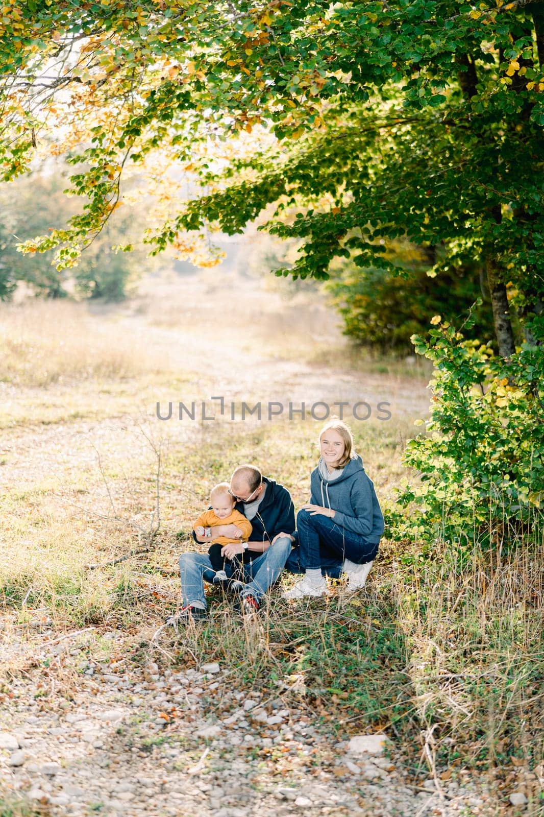 Mom squatted down next to dad sitting with a little boy in his arms. High quality photo