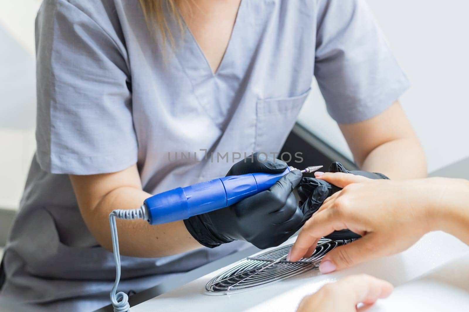 Manicurist uses an electric drill to remove old gel polish from nails. A woman is getting a manicure of nails. The beautician files the client's nails. professional manicure tool. Close-up.