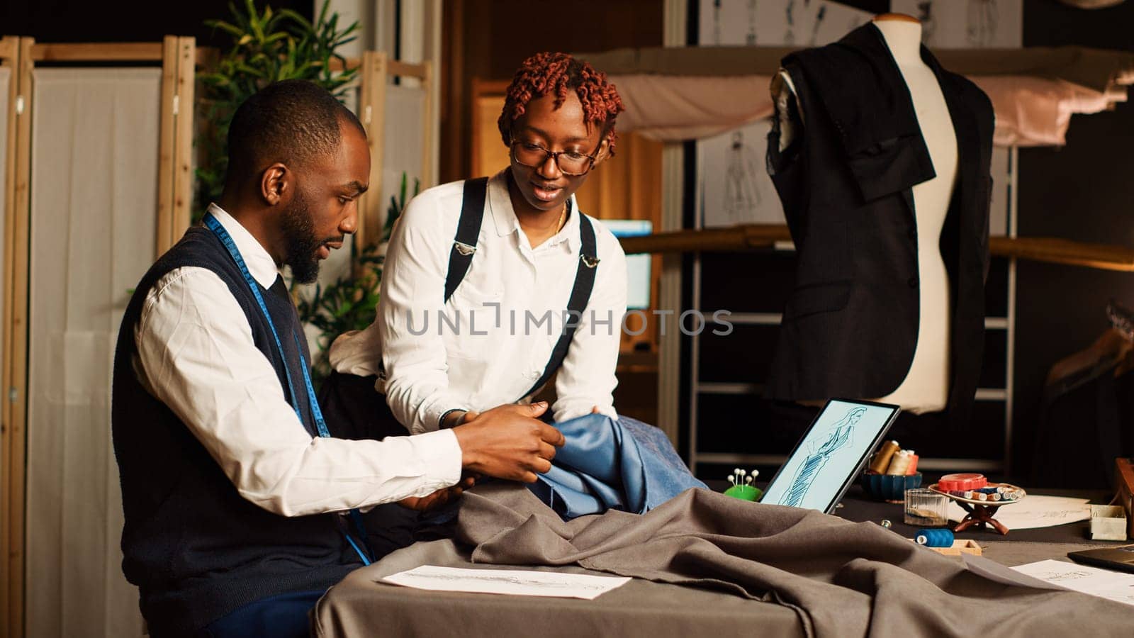 Couturiers team choosing fabric to craft tailored clothes, working in atelier to manufacture fashion items for clothing line. Two tailors picking material, handcraft process. Tripod shot.