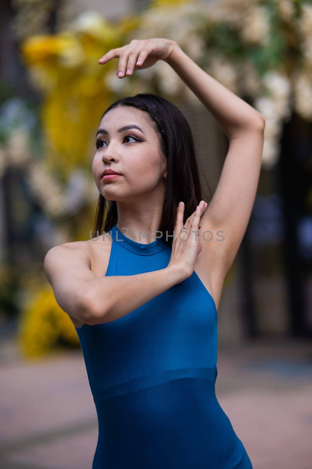 Close-up portrait of a beautiful Asian ballerina posing against the background of a building decorated with flowers. Vertical photo. by mrwed54