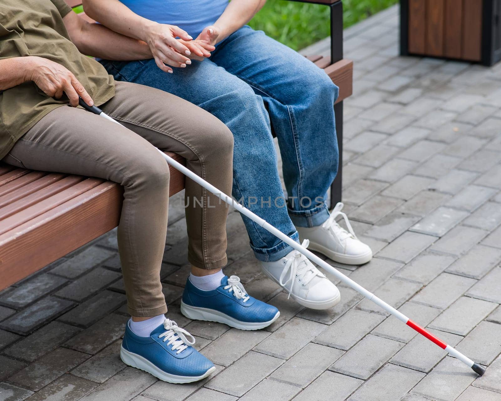 An elderly blind woman and her pregnant daughter are sitting on a bench in the park. Close up legs