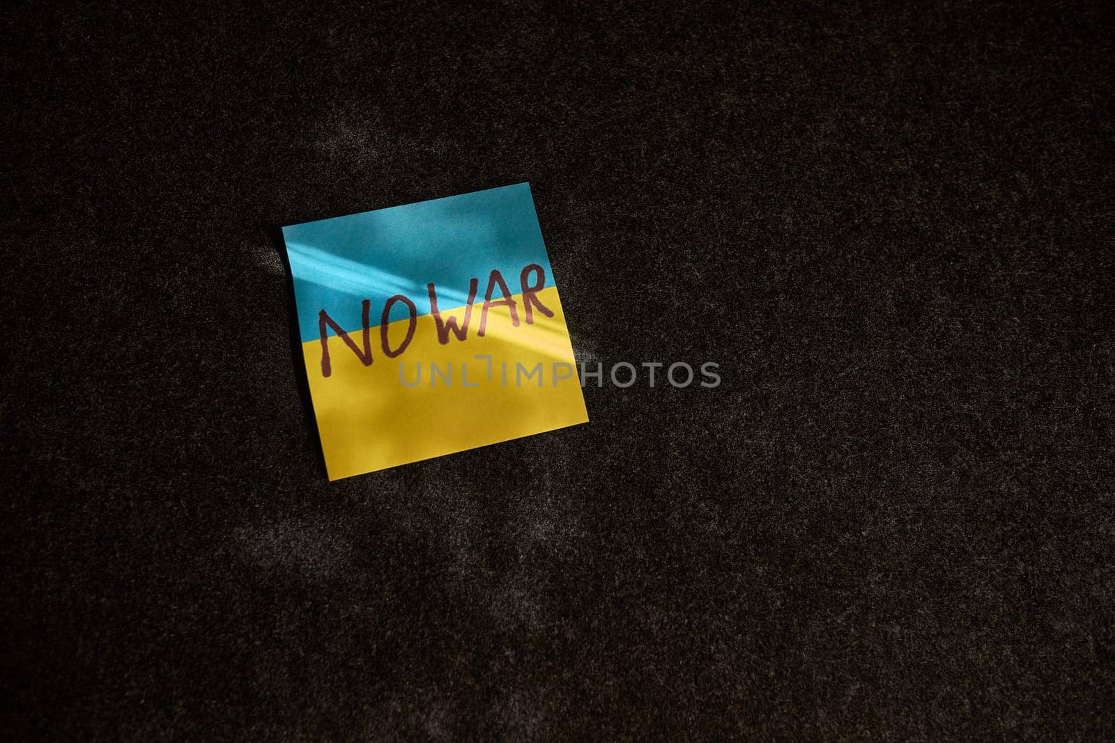 The sticker in the form of the Ukrainian flag lies. on a dark surface and a ray of sunlight falls on it by snep_photo