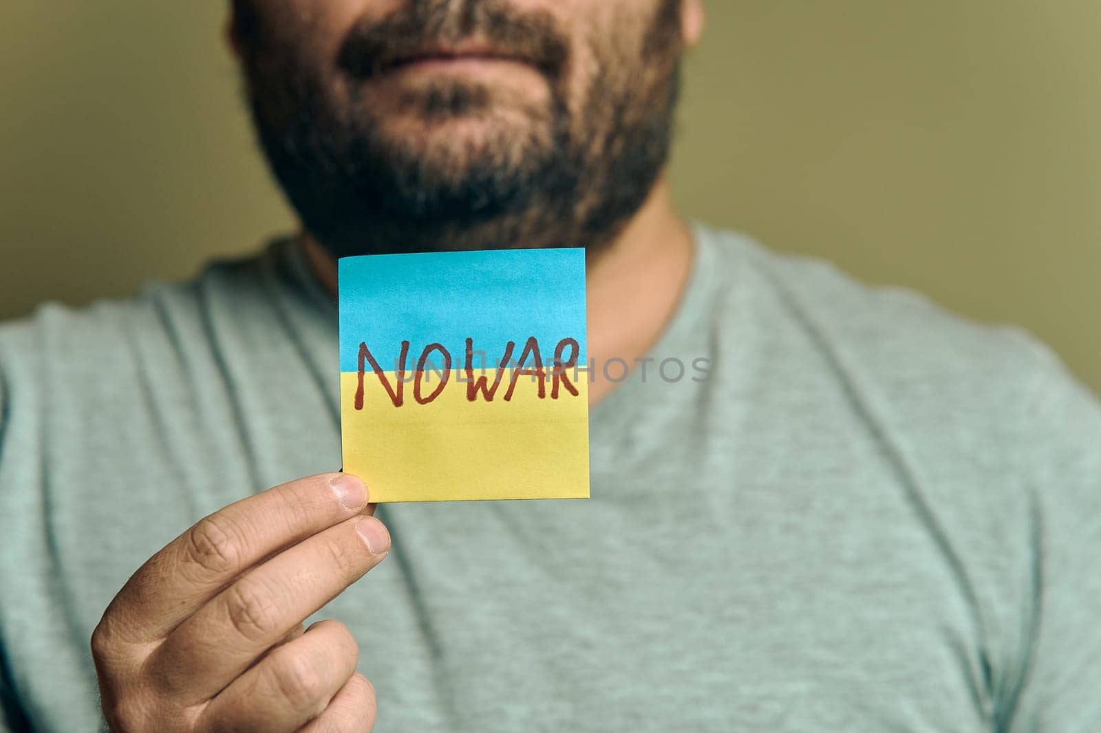 A bearded European man holds a sticker in front of him, in the form of a Ukrainian flag with the inscription no war by snep_photo