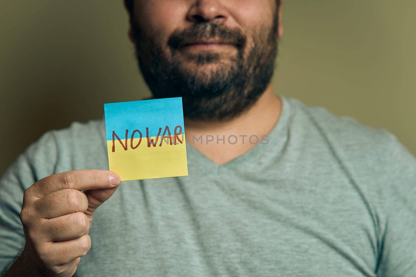 A bearded European man holds a sticker in front of him, in the form of a Ukrainian flag with the inscription no war